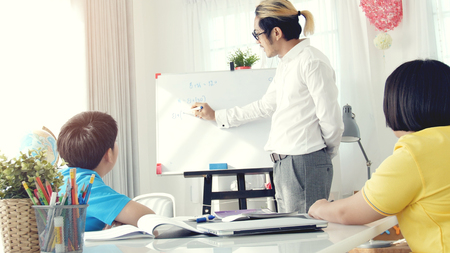 Tutor room children in class writing on board with teacher. Asian child learning with teacher at home.の写真素材