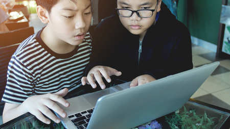 Happy asian boy typing  on laptop computer.