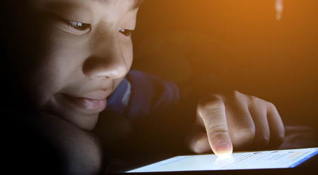 Young asian boy playing with a cellphone or smartphone on a bed. nightの写真素材