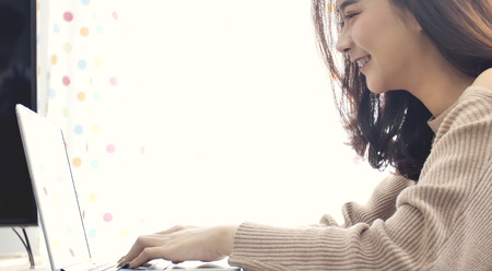 Asian girl typing on laptop computer . Cute THAILAND woman model using laptop with smile face .の写真素材