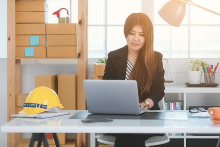 Portrait of a cheerful businesswoman sitting at the table in office and talking with smile face. Safety helmet in office.の写真素材