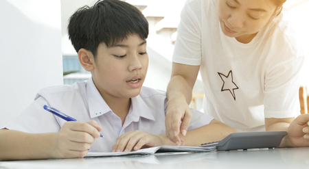 Asian mother helping her son doing homework on white table.の写真素材