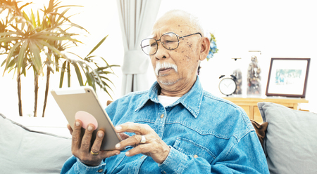 Asian Senior man with white mustache using tablet computer at home, Happy grandfather with technology in handの写真素材