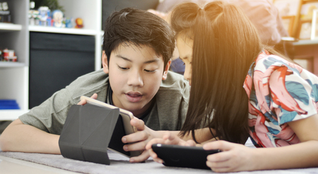 Children playing tablet or smartphone at home , Asian boy and girl playing game on mobile phone together with smile face.の写真素材