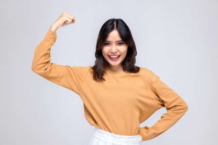 Portraits of young Asian women. Raise arms. With a smiling face happily, a beautiful woman with a sense of self-confidence, looks good, happy on a gray background.の写真素材