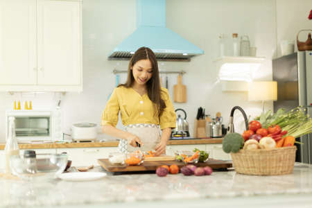 Woman cooking rice with vegetables in kitchenの写真素材