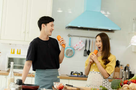 Young asian happy active family couple dancing laughing together preparing food at home, carefree joyful husband and wife having fun cooking healthy romantic dinner meal listen to music in kitchen.の写真素材