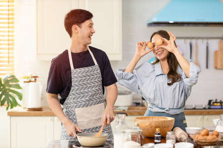 Asian couple Help each other to make a bakery In a romantic atmosphere in the kitchen at home. Young women help cook holiday with smiling and happy faces.の写真素材
