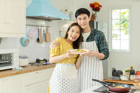 Portrait young couple in love helping to cook In a romantic atmosphere at home and looking at camera with smile face.の写真素材