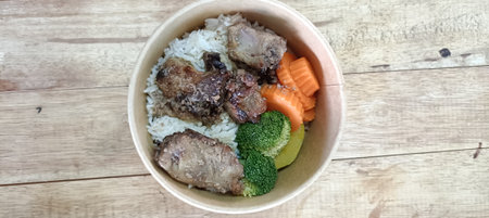 Rice with pork and carrot in brown bowl on wooden table.の写真素材