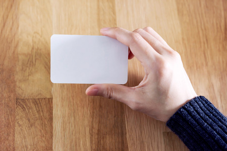 Woman holding blank business card for mock up, present over wooden desk backgroundの写真素材