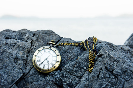 vintage golden pocket watch on island rock, blurred sea as backgroundの写真素材