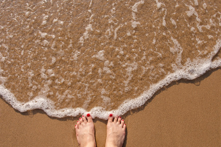 Red nail Feet of female stand on the summer sand beach, top view, Woman solo travel conceptの写真素材