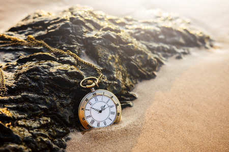 Vintage pocket watch on golden sand beach during sunrise or sunset in summer, Time conceptの写真素材