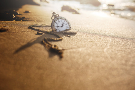 Vintage pocket watch on golden sand beach during sunrise or sunset in summer, Time concept