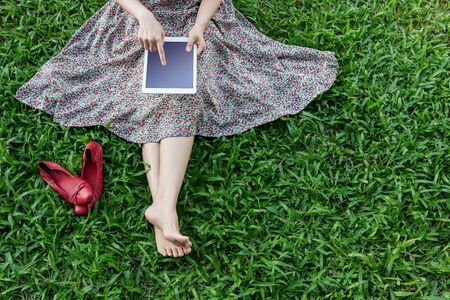 Woman relaxing on green grass and using tablet in Spring time, Top view, Tablet screen is clipping pathの写真素材