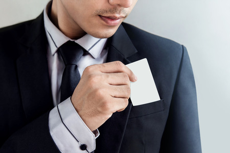 Upper part of Businessman in black suit pulling blank business card from his pocket, Selective focus on face and hand, card as clipping pathの写真素材