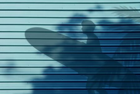 Blue aluminum alloy wall texture background with shadow of male bring surf board to the beachの写真素材