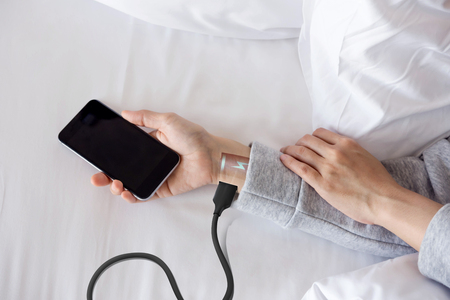 Overuse and tired Android Robot woman or Future human lay on bed with Low battery and charge via electric cable on arm, Smart phone addict and need to rest concept, Top view, Day lightの写真素材