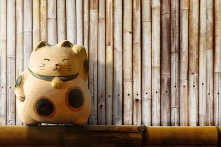 Japan Maneki Neko or beckoning cat, mascot of lucky and money, Present over bamboo fenceの写真素材