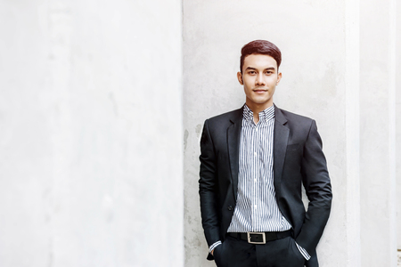 Smart Asian Businessman in Formal Suit, Looking at Camera and Smiling in Outside Buildingの写真素材