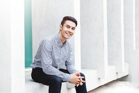 Smart Asian Businessman in Casual Dress, Looking at Camera and Smiling in Outside Buildingの写真素材