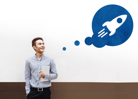 Start Concept, Happy Young Asian Businessman Smiling and Looking above at Think Bubble with Rocket Startup icon, Dreaming for Successの写真素材