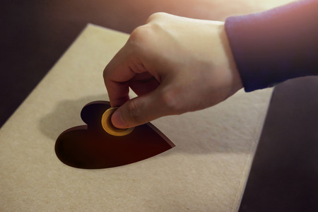 Donation Concept. Hand putting Money Coin into a Heart Shape hole on Donate Boxの写真素材