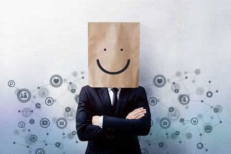 Customer Experience Concept, Portrait of Happy Businessman Client with Smiley Face Emotion on Paper Bag, Crossed arms and wearing Suit, Standing at the Wall with Social Network Iconsの写真素材