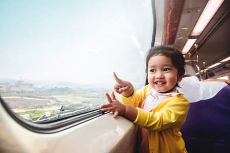 Happy and Excited Kids Traveling by Train. A Two Years old Girl Pointing her hand to Outside View, Sitting Near Wide Glass Window and Smilingの写真素材