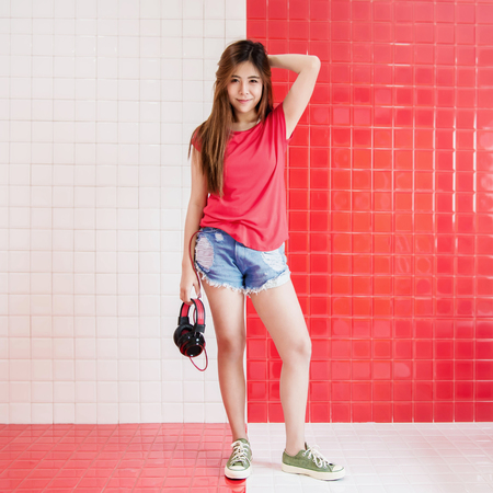 Happy Young Woman Standing with Headphone to Listen the Music in the Room, Looking at Camera with Charming Eyesの写真素材