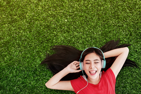 Happy Young Woman Lay on Green Grass to Listening Music via Headphone in the Park. Smiling and Closed Eyes, Top Viewの写真素材