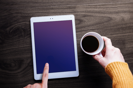 Digital Tablet Mockup Image. Screen as Clipping Path. Woman Touching on a Display while Drinking Coffee, Wooden Table, Top Viewの写真素材