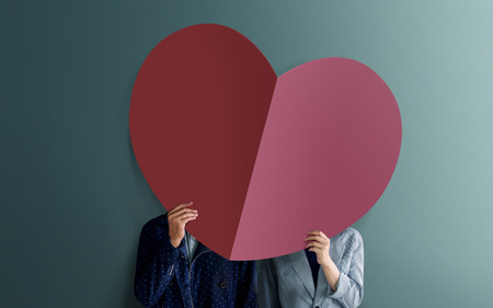 Love and Valentines Day Concept. Young Couple Standing at the Wall and Covered Face by Paper Heart Shape. Bright Color Tone. Romantic Situation in Relationshipの写真素材