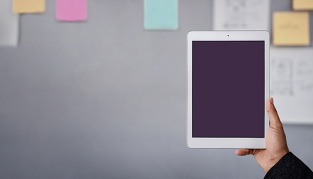 Tablet Mockup Image. Display Screen is Clipping Path. Modern Businesman Using Tablet in Office. Blurred Sticky Note and Project Planning on the Wall as backgroundの写真素材