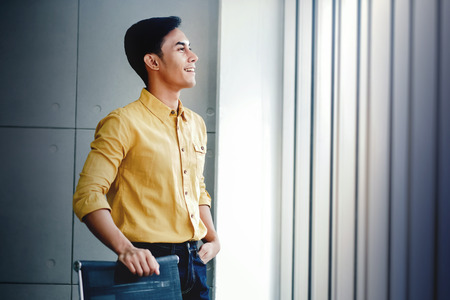 Portrait of Happy Businessman Standing by the Window in Office. Looking Away and Smiling. Dreaming for Successの写真素材