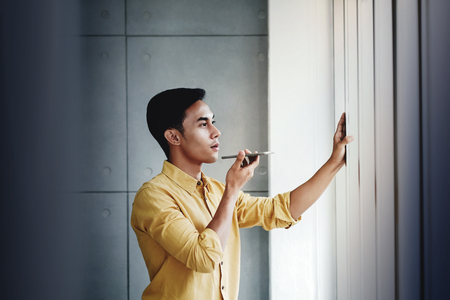 Young Businessman Standing by the Window in Office. Using Voice Control via Smartphoneの写真素材