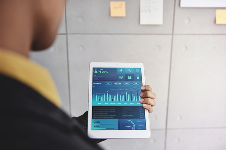 Technology in Finance and Business Marketing Concept. Graphs and Charts show on Touch Pad's Screen in. Modern Businessman seeing Statistical Data on Digital Tablet in Office Meeting Room. Over the Shoulder Viewの写真素材