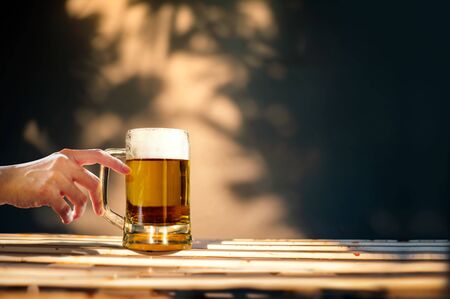 a Glass of Beer on Table in Summer Sunny Day. People Drinking Brew. Shadow of Tree as backgroundの写真素材