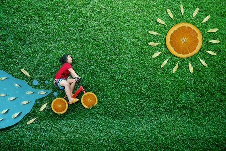 High Angle View of a Happy Asian Kids. Girl on Bicycle Lay Down at Green lawn in Summer Sunny Day....
