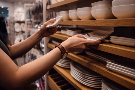 Customer Compared Products from Rack in the Shop. Young Woman Choosing Dishware in Household Store....