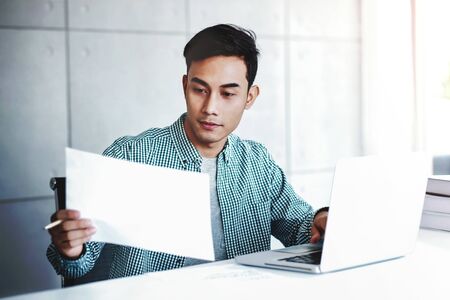 Happy Young Businessman Working on Computer Laptop and Document Paper in Office