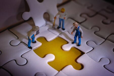 Teamwork and Solving Problem Concept. Group of Miniature Worker Men Found Something Wrong on the Work Process (a Piece of Jigsaw Puzzle)の写真素材