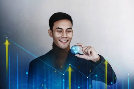 Globalization and Worldwide Business Marketing Concept. Happy Smiling Businessman holding a Transparent Blue World Globe in Hand. Surrounded by Positive Graph Chartの写真素材