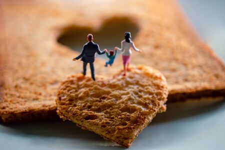 Love Concept. Miniature of Happy Family Walking on Burned Sliced Toasted Bread with a shape of Heartの写真素材