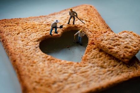 Love Concept. Sad Relationship. Group of Worker Miniature Fixing a Burned Sliced Toasted Bread with a shape of Heartの写真素材