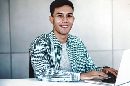 Smart Young Asian Businessman Working on Computer Laptop in Office. Smiling and looking at Cameraの写真素材