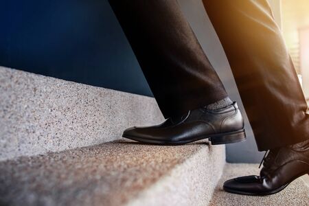 Motivation and challenging Career Concept. Steps Forward into a Success. Low Section of Businessman Walking Up on Staircase. Male in Black Formal Dressの写真素材
