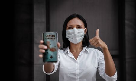 Technology for Covid-19 or Corona Virus Situation Concept. Business Woman with Medical Mask Presenting the Application for Virus Tracking on Mobile Phone. Helping People to Deal with itの写真素材