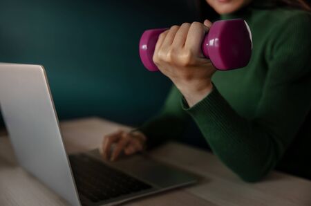 Work Life Balance Concept. Young Employee Woman Exercising with Dumbbell  while Working on Computer Laptopの写真素材